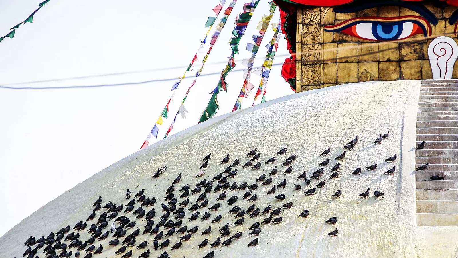 The golden spire of Boudhanath Stupa strung with colorful Tibetan prayer flags against a grey sky