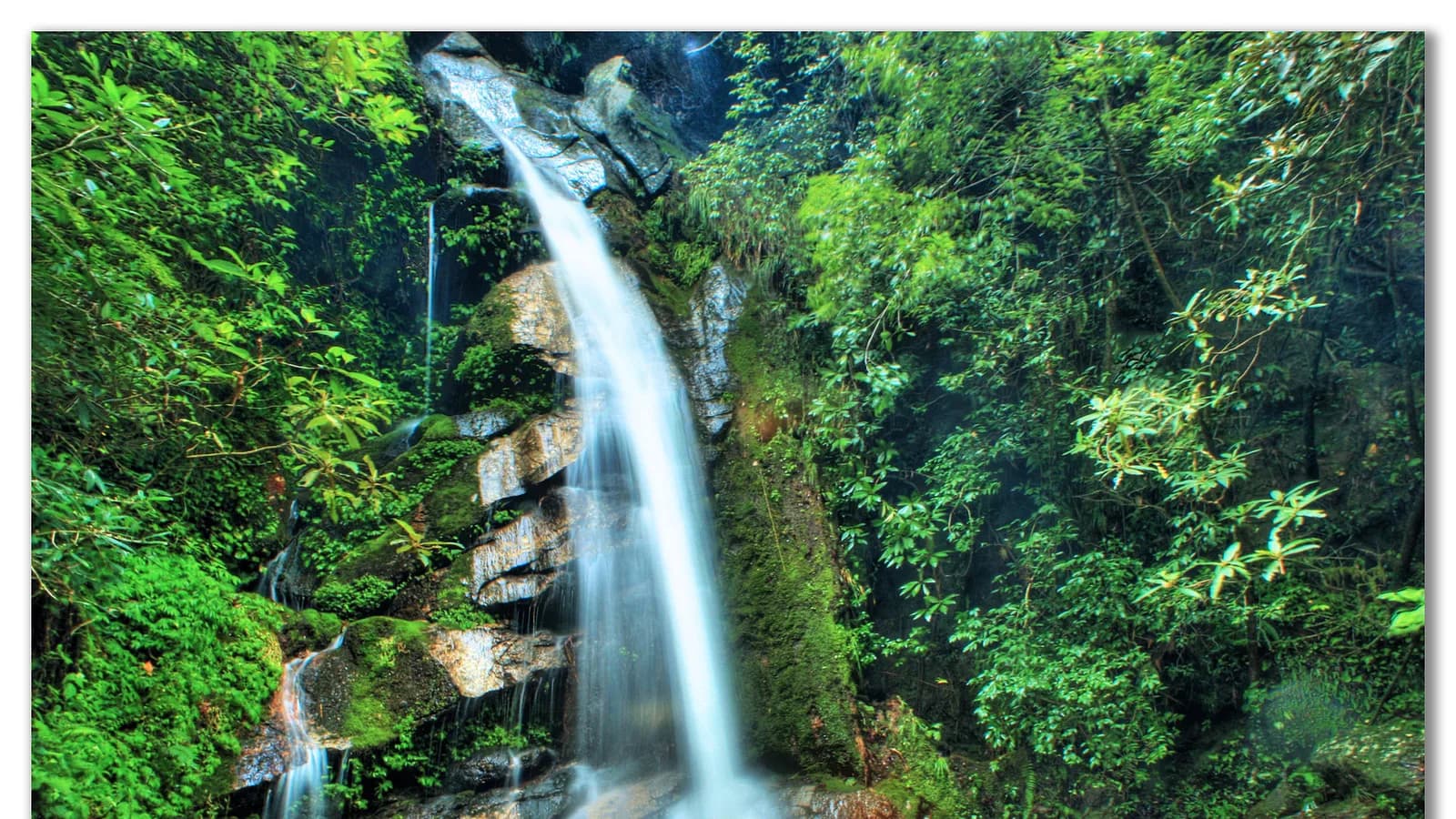 A tall waterfall cascading over mossy rocks through lush green forest at Sundarijal, Nepal