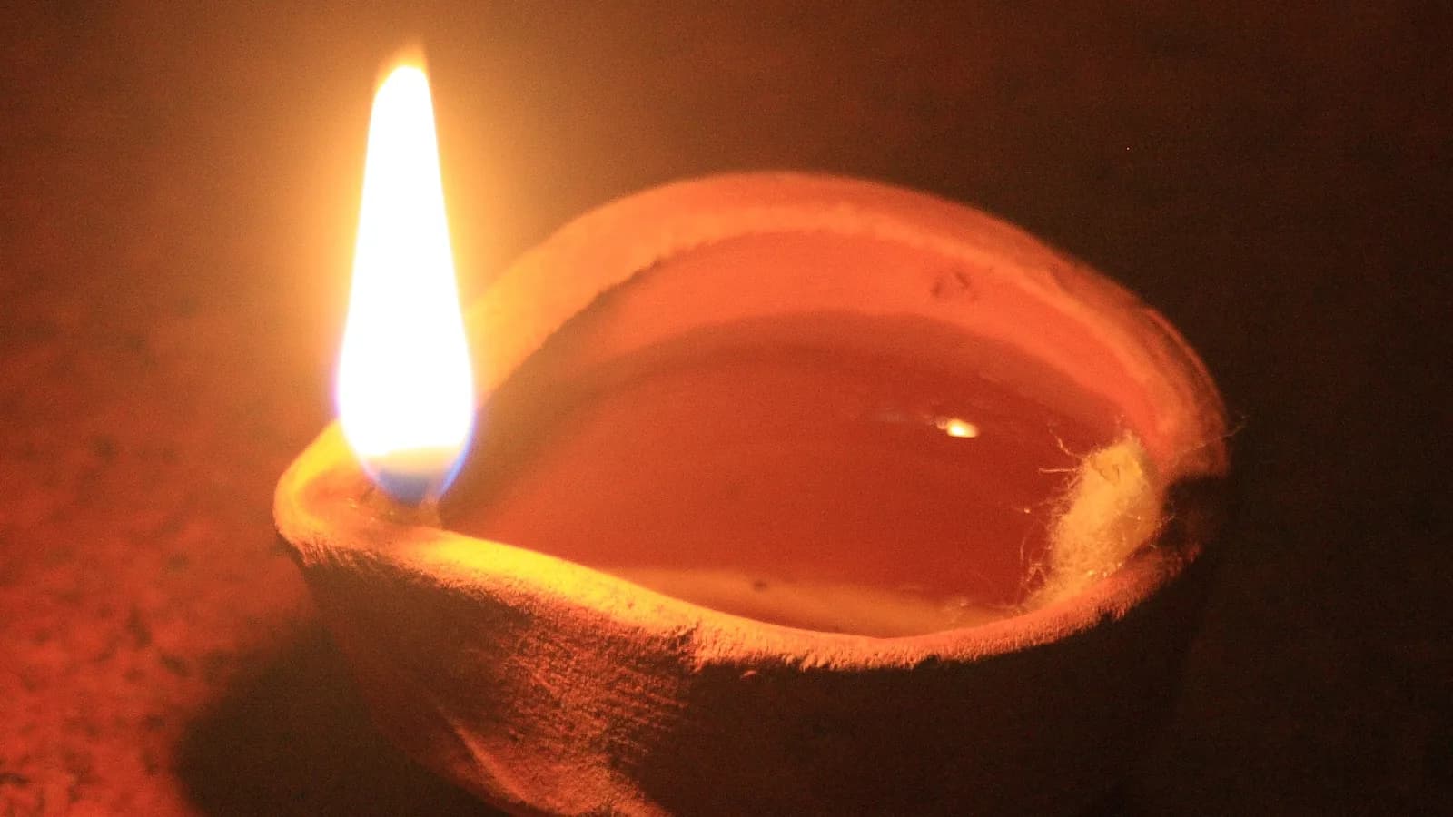 A small clay diya oil lamp lit for the festival of lights, its flame glowing against a dark background