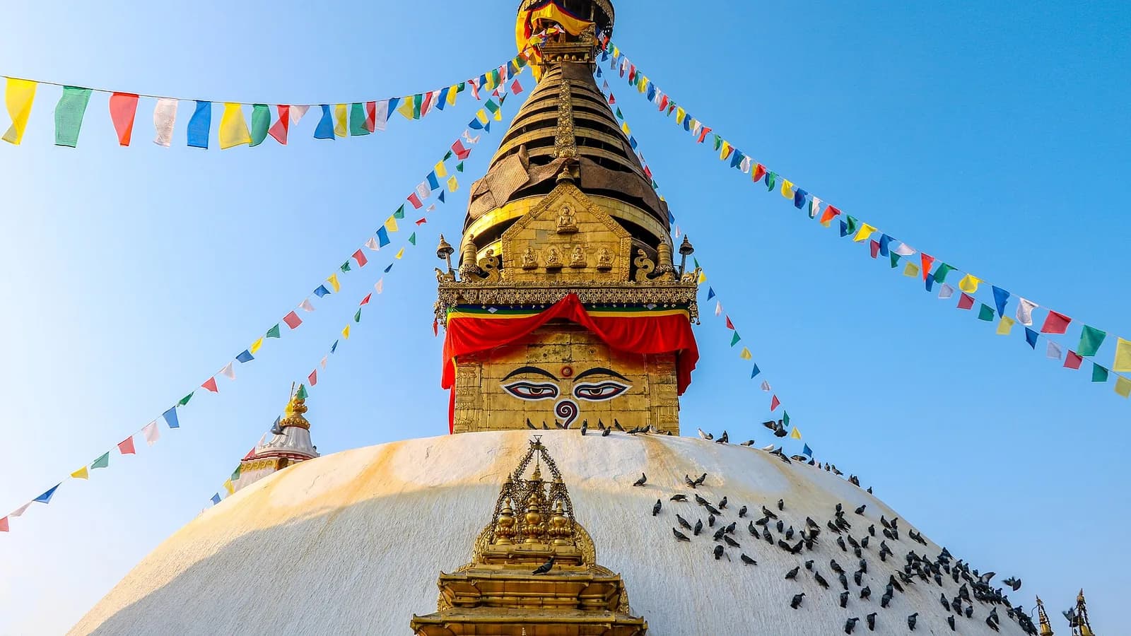 The white dome and golden spire of Swayambhunath stupa with the painted Buddha eyes, perched on a green hill above the Kathmandu Valley