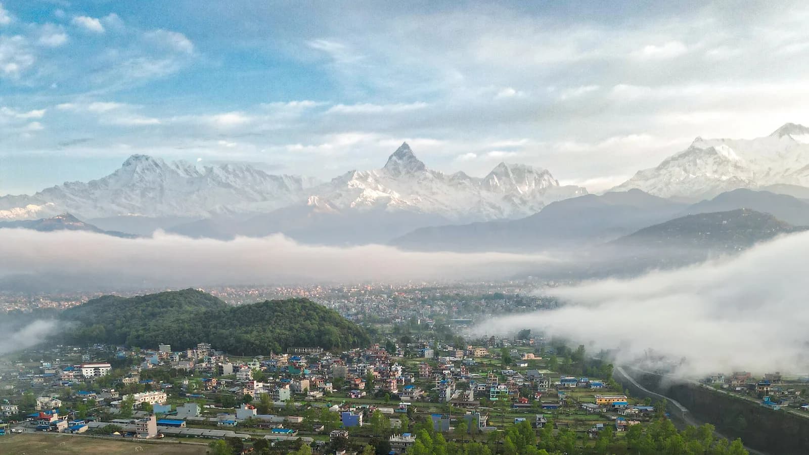 The Pokhara valley in Nepal, ringed by green hills with Himalayan peaks behind, near the region's mountain biking trails