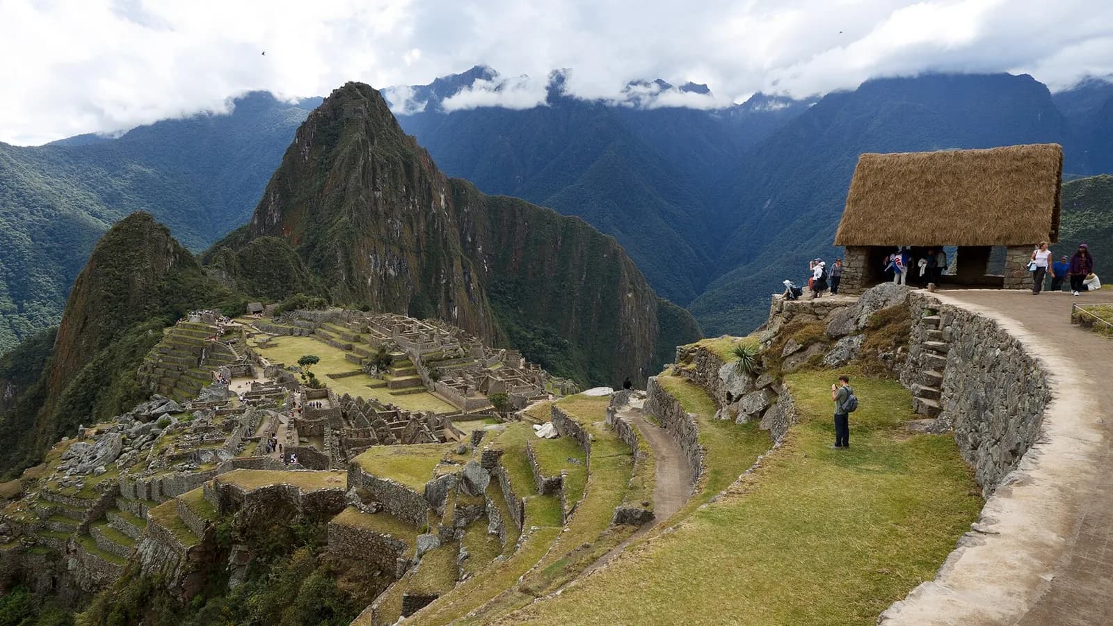 The stone ruins of Machu Picchu on a green mountain ridge with steep Andean peaks rising behind