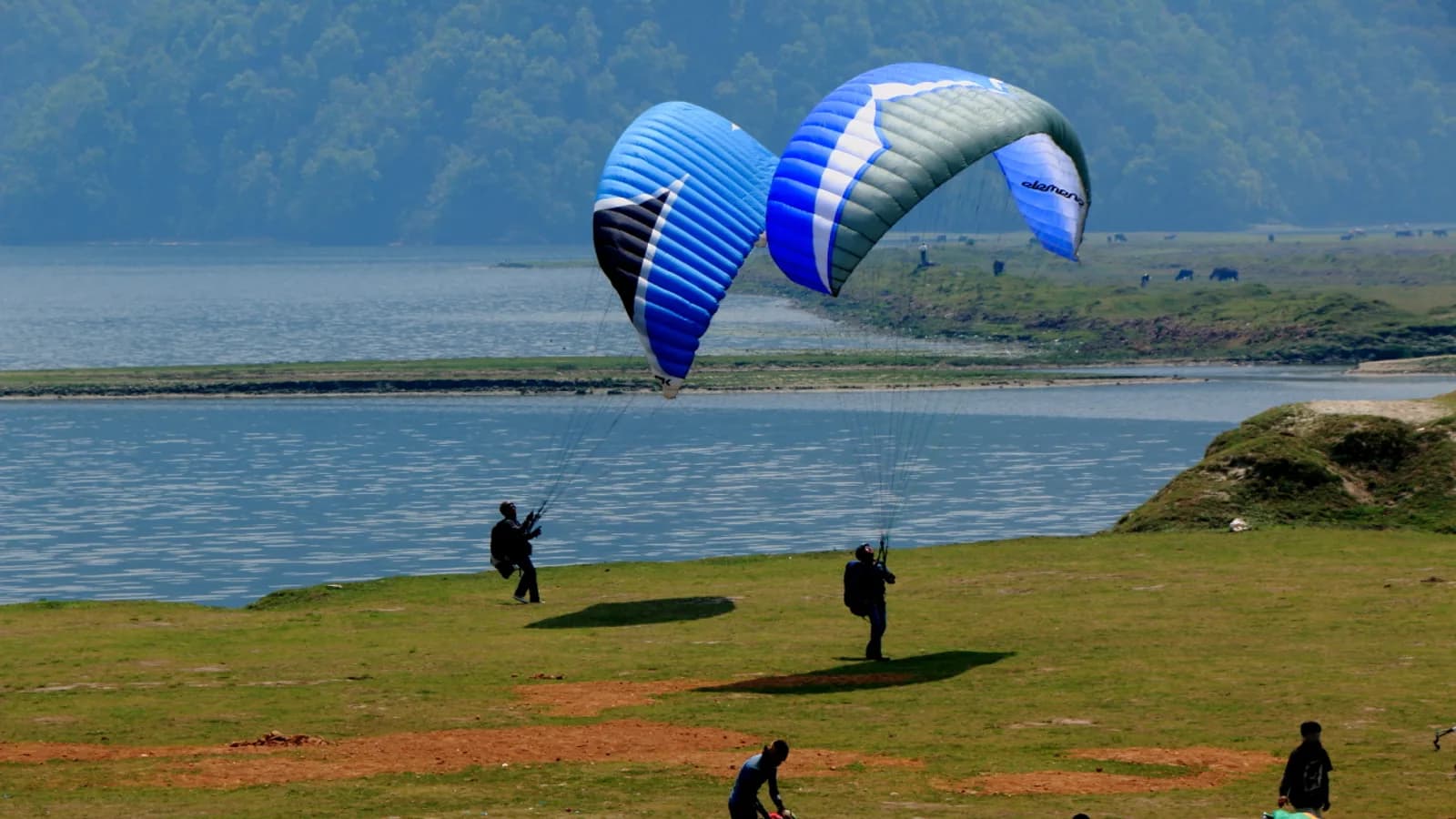 A tandem paraglider soaring above Phewa Lake at Pokhara with the hills behind